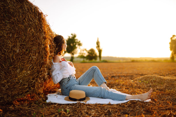 幸福的女人附近的草垛在日落。图片下载