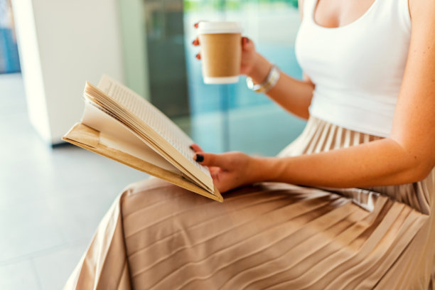 女人手里拿着书和咖啡。素材图片