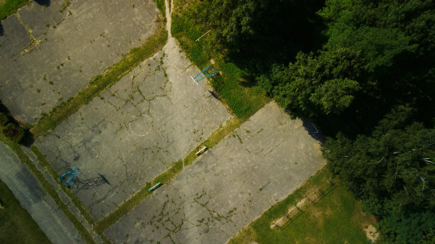 一个城市街区里的旧学校体育场。沥青和运动器材开裂。多层建筑和大片绿地。航空摄影。图片下载