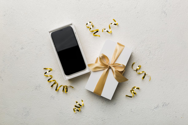 打开礼品盒，金色丝带和智能手机彩色背景，俯视图。空白开箱包装模型，模板为您的设计品牌模型图片下载