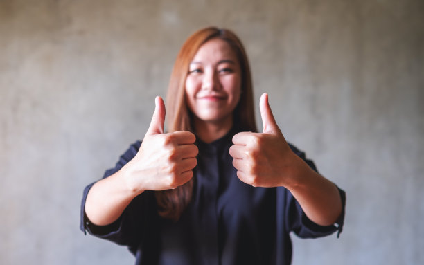 一个年轻的亚洲女人做和显示大拇指向上的手势图片下载