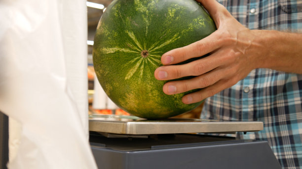 商店磅秤和一名男子称熟西瓜的特写图片下载