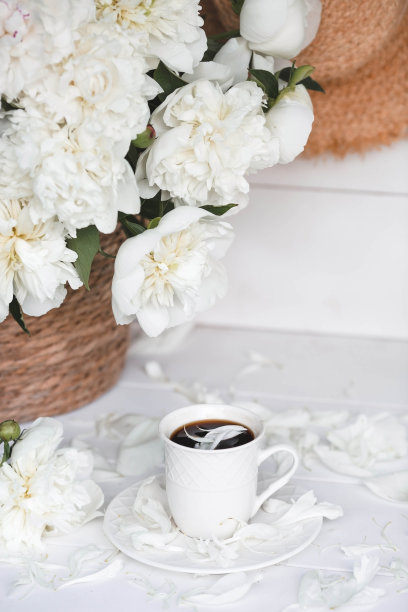 一个漂亮的明信片。一个白色咖啡杯和一个茶托，蜡烛和一个插着一束白色牡丹的花瓶。美丽的生活。春天,夏天的时间。“早上好”的概念。图片下载