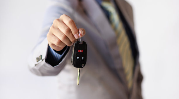 商人之手微笑的汽车推销员递上你的新车钥匙，经销商和销售给汽车钥匙的概念图片下载