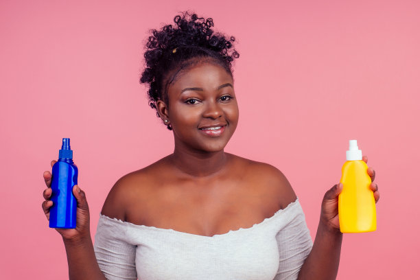 非洲裔美国妇女应用奶油shoosing之间的两个产品在工作室粉红色的背景图片下载