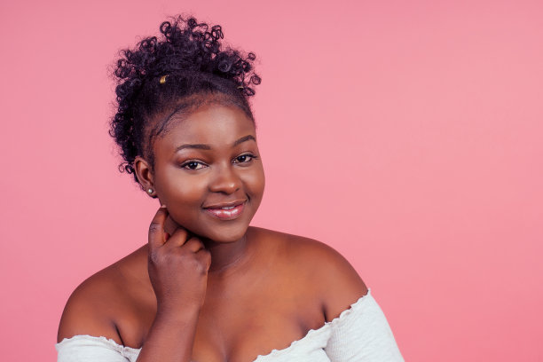 美丽的非洲女人与完美的皮肤卷发看ca，时代在粉红色的工作室背景图片下载