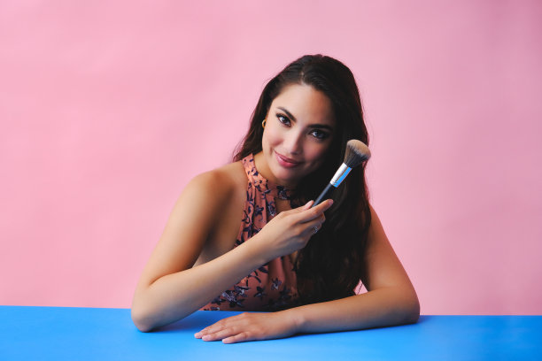 年轻的成年拉丁美女与化妆刷的工作室背景图片下载