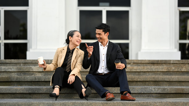 积极成熟的女商人和年轻的商人坐在办公楼的楼梯上聊天。图片下载