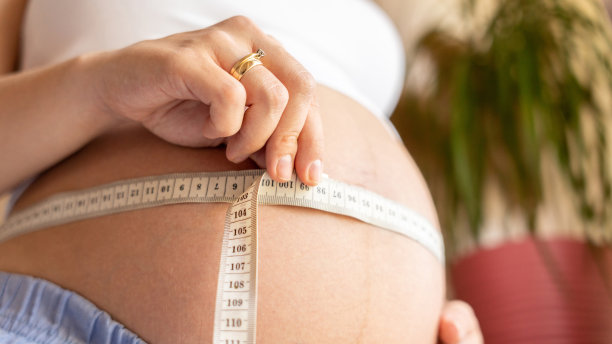 测量孕妇身体。幸福美丽的孕妇用卷尺量肚子。怀孕的概念，母性，对婴儿的期望。图片下载