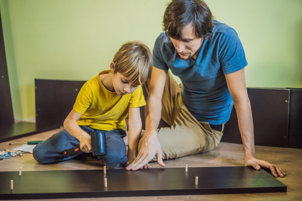 父子俩在组装家具。男孩在家帮他爸爸干活。幸福的家庭的概念图片下载