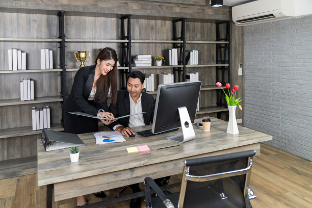 站着聪明的女秘书拿着文件现在老板经理坐在男人看着文件纸在她的手在现代木制办公室。快乐的亚洲商人一起工作。图片下载