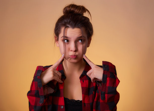 深色头发的女人撅着嘴做鱼脸或鸭脸鬼脸，耍弄，做可笑的幼稚滑稽的鬼脸。室内工作室拍摄孤立的粉红色背景图片下载
