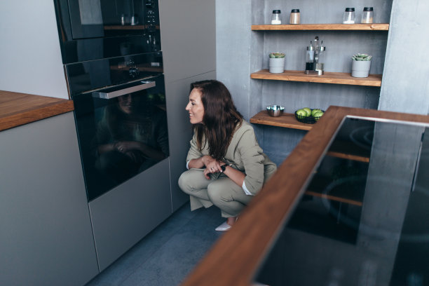 女人透过玻璃看烤箱里正在煮的食物图片下载