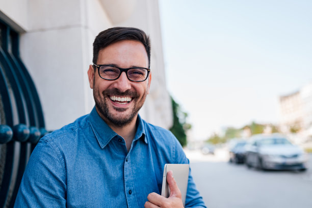 微笑的商人带着笔记本电脑坐在城市的墙上图片下载