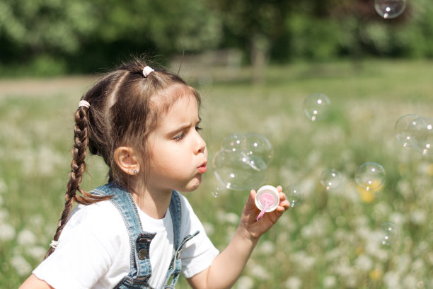 一个快乐的白人小女孩的肖像吹肥皂泡在一个夏天的公园。夏天,童年的概念。图片下载
