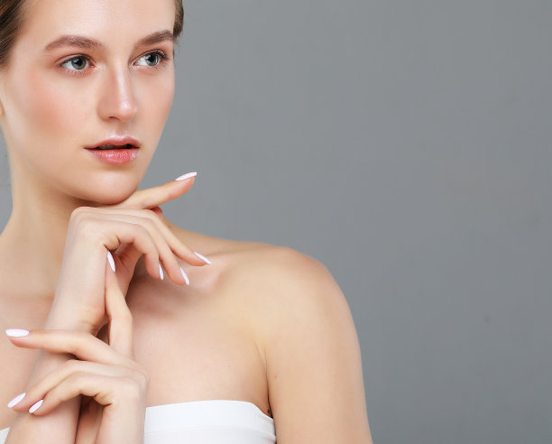 美丽的年轻女子与清洁新鲜的皮肤触摸她的脸在灰色的背景。图片下载