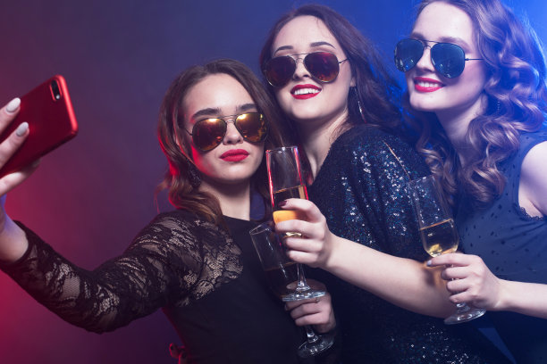 一群参加派对的女人一边吹着笛子，一边喝着气泡酒自拍。图片下载
