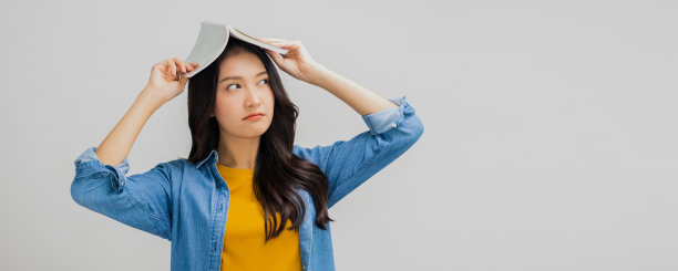 美丽的亚洲女人无聊和拿着书在她的头上，疲惫和无聊的年轻女孩学生图片下载