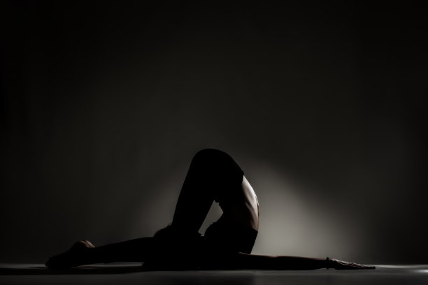 适合芭蕾舞女孩躺着和伸展练习瑜伽姿势。侧面点燃剪影对黑暗的背景…图片下载