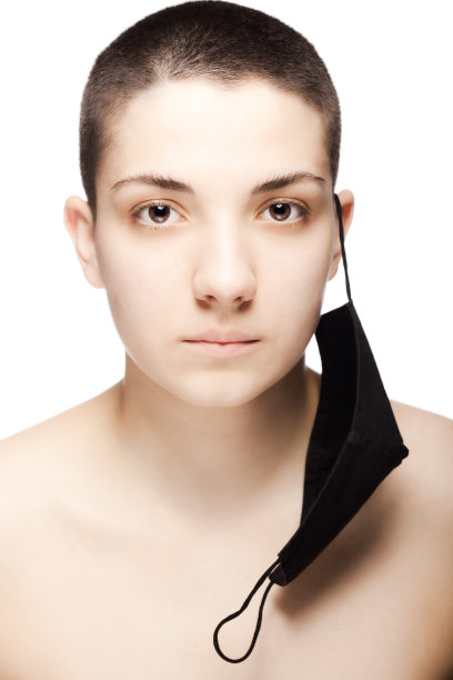 可爱的女孩，很短的头发，戴着黑色的防护口罩挂在她的耳朵上。工作室肖像孤立在白色背景..图片下载