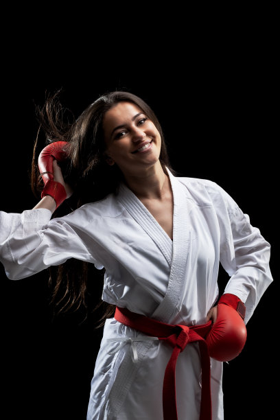 美丽快乐的女孩女孩摆姿势和微笑在空手道服装和服和红色手套对黑色背景。图片下载