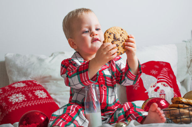 可爱的蹒跚学步的小男孩穿着睡衣在家吃圣诞饼干的特写。新年在家舒适，卧室装饰。。图片下载