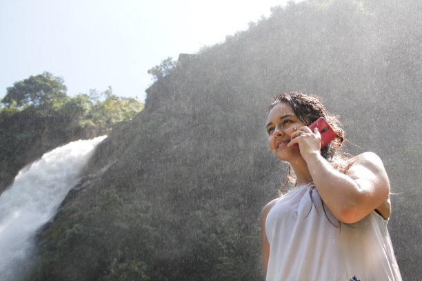 美丽的年轻女子享受着瀑布和打电话图片下载