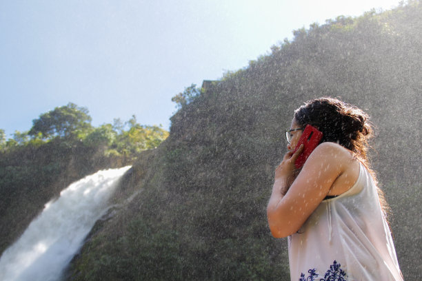 年轻女子在瀑布边观看，打电话工作和旅行图片下载