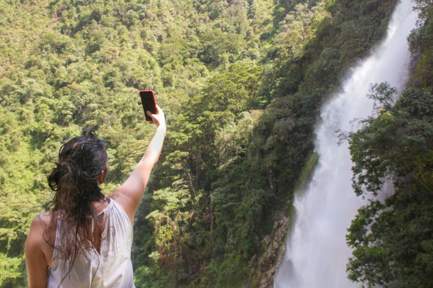 美丽的年轻女子在拍摄瀑布的照片图片下载