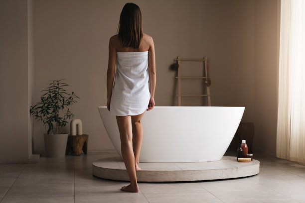 背影苗条的女人穿着毛巾站在浴缸附近的时尚浴室图片下载