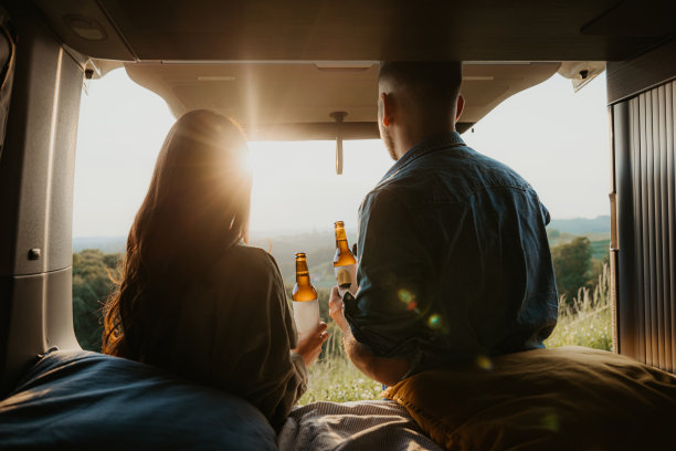 一对情侣站在外面看着对方，两人都靠在自己的面包车上，拿着一个啤酒瓶，面包车后门打开图片下载