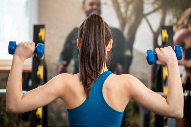 美丽的年轻女运动员在健身房举重。库存照片图片下载