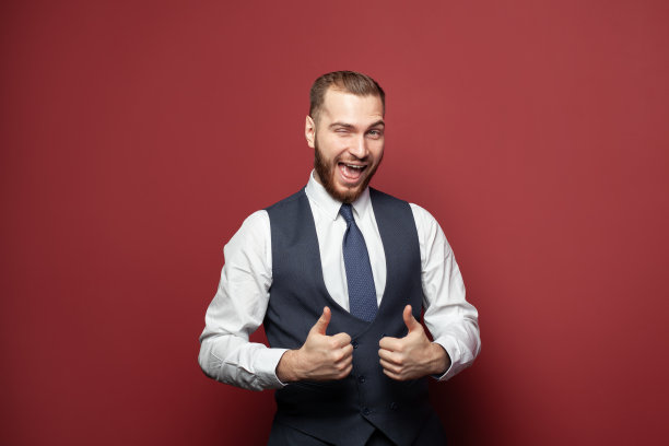 兴奋的成功商人对着工作室红色墙壁的背景眨眨眼睛，竖起大拇指图片下载