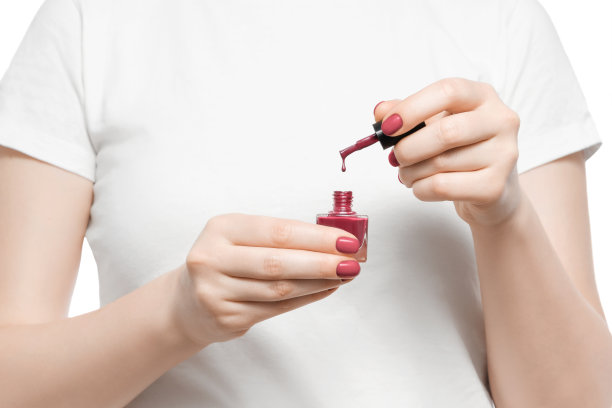 一个穿着白色t恤的女人拿着红色指甲油，刷子上挂着一滴指甲油。图片下载