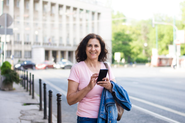 成熟的女人在城市里等出租车，用她的智能手机图片下载