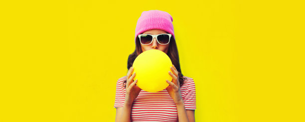 时髦的酷年轻女子膨胀口香糖的时尚肖像戴粉红色的帽子在黄色的背景图片下载