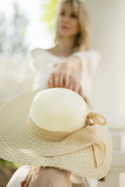 一名白衣女子坐在室外的走廊上，膝盖上戴着草帽图片下载