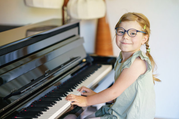 漂亮的学龄前女孩在客厅弹钢琴。可爱的学龄前儿童戴着眼镜，玩着学习乐器的乐趣。儿童早期音乐教育图片下载