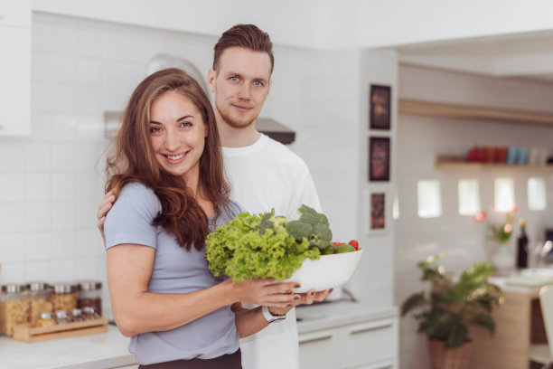 幸福的夫妻喜欢一起在厨房做饭。年轻可爱的男女站在白色的厨房里。图片下载