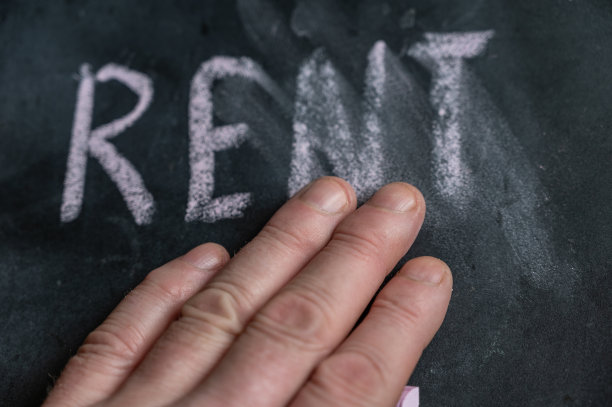 黑色黑板上半擦去的“RENT”字。一名成年男子的左手用手指擦掉了手写的单词。黑色表面模糊的字母。图片下载