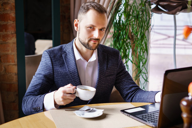 一个西装革履的年轻人坐在餐馆的一张桌子旁。在餐馆或咖啡馆用笔记本电脑工作的商人喝着咖啡图片下载