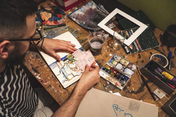 一个戴眼镜的家伙在工作室里把图片和图画粘贴在笔记本上。Craftbooking。艺术。图片,绘画图片下载