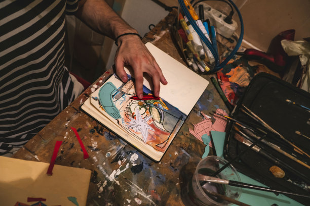 在工作室里把图画和图片粘贴在笔记本上的人。Craftbooking。艺术。图片下载