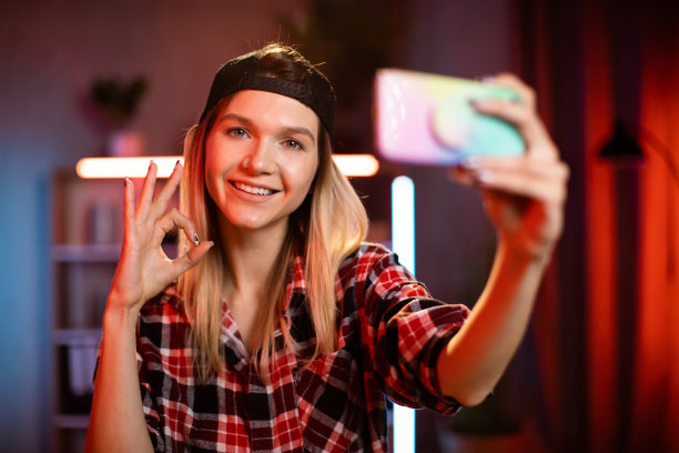 可爱的年轻女子戴着黑色的帽子，在家里用现代智能手机自拍。图片下载