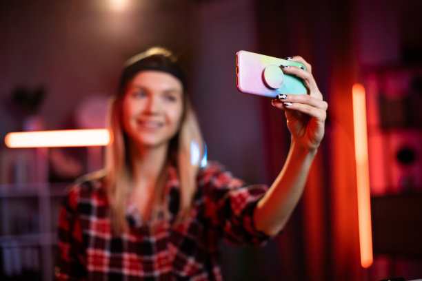 可爱的年轻女子戴着黑色的帽子，在家里用现代智能手机自拍。图片下载