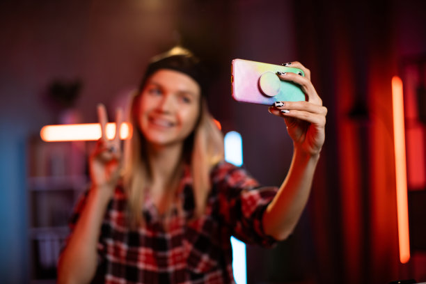 可爱的年轻女子戴着黑色的帽子，在家里用现代智能手机自拍。图片下载