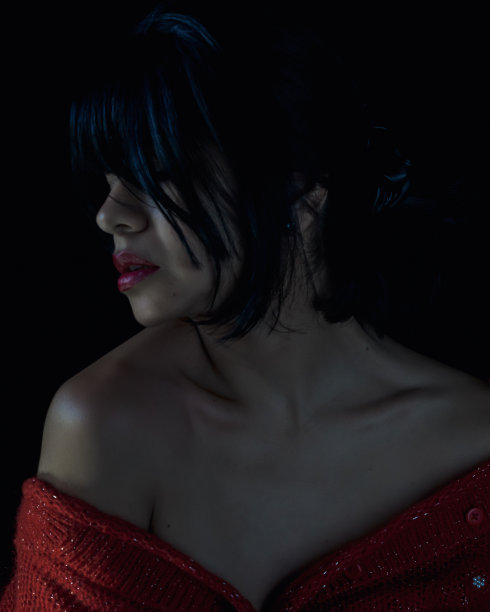 迷人的深黑色拉丁女人的肖像在侧面裸露的肩膀，红色的嘴唇和黑色的头发。黑色背景的工作室照片。图片下载