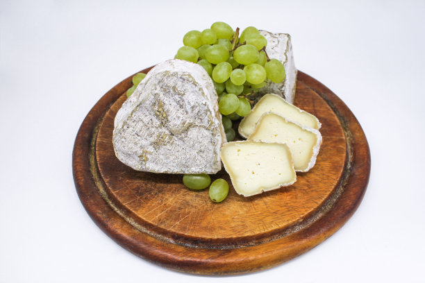 各种发霉的蓝色奶酪，山羊牛奶放在木制砧板上，还有绿色的葡萄。白色背景图片下载