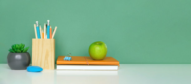 学校设备上白色的桌子，绿色的墙壁背景。教育背景。木制的学校用品，笔记本，铅笔和仙人掌植物。回到学校。学生的桌子上。文具进行研究。在家里工作素材图片
