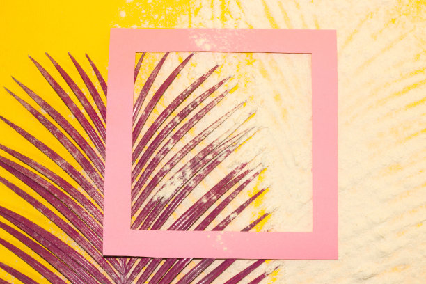 黄色背景以沙滩沙和粉色框架作为复制空间，角落的粉色棕榈叶，创意现代热带背景图片下载